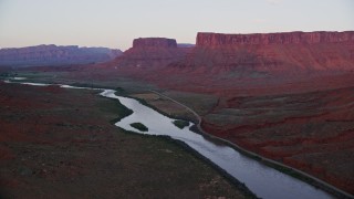 AX138_403E - 5.5K aerial stock footage video follow Colorado River and State Route 128, mesas in background, Moab, Utah, sunset
