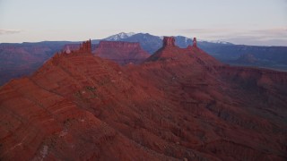 AX138_410E - 5.5K aerial stock footage of passing by buttes and Castleton Tower, Moab, Utah, sunset