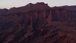 AX138_432E - 5.5K aerial stock footage of flying by Cottontail Tower, Echo Tower, The Titan at base of mesa in Fisher Towers, Utah, sunset