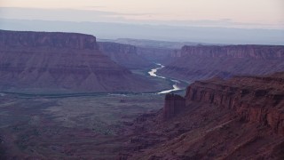 AX138_447E - 5.5K aerial stock footage of flying by Colorado River and a canyon, Fisher Towers, Utah, twilight