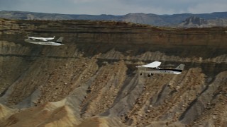 AX139_077E - 5.5K aerial stock footage of tracking Tecnam P2006T and Cessna flying by desert mesas, Grand County, Utah