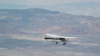AX139_126E - 5.5K aerial stock footage of Cessna airplane flying high above desert, partly cloudy, Emery County, Utah