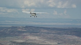 AX139_129E - 5.5K aerial stock footage of focusing on a Cessna airplane flying high above desert, partly cloudy, Emery County, Utah
