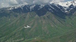 AX140_125E - 5.5K aerial stock footage track a Tecnam P2006T passing a snowy mountain peak, Wasatch Range, Utah