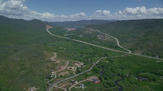 AX140_185 - 5.5K aerial stock footage of flying by Highway 40 through green mountain foothills and homes, Heber City, Utah