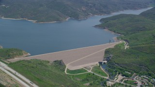 AX140_191 - 5.5K aerial stock footage of a dam surrounded by green hills, reveal the highway, Jordanelle Dam, Utah