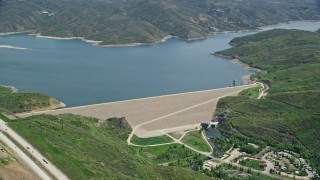 AX140_191E - 5.5K aerial stock footage of orbiting dam surrounded by green hills near highway, Jordanelle Dam, Utah