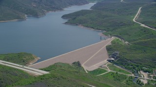 AX140_192 - 5.5K aerial stock footage of orbiting dam surrounded by green hills near highway, Jordanelle Dam, Utah