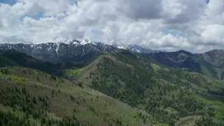 AX140_230 - 5.5K aerial stock footage of passing green mountains with snowy peaks in the distance, Wasatch Range, Utah