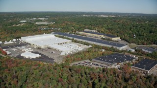 AX142_001E - 5.5K aerial stock footage flying by warehouses surrounded by trees in autumn, Westwood, Massachusetts