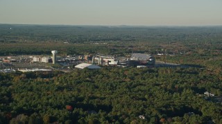 AX145_112E - 6k aerial stock footage flying by Gillette Stadium, dense trees, autumn, Foxborough, Massachusetts