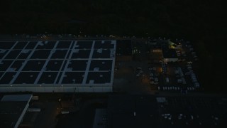AX146_160E - 6k aerial stock footage flying by a large warehouse, Hyde Park, Massachusetts, night