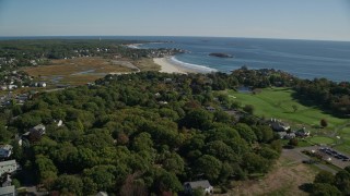 AX147_106 - 6K aerial stock footage flying over trees and coastal community toward beaches, Gloucester, Massachusetts