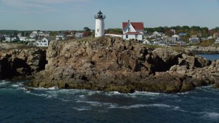 AX147_241 - 6k aerial stock footage flying low over water, tilt up to reveal Cape Neddick Light, York, Maine