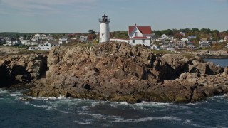 AX147_241E - 6K aerial stock footage flying low over water, tilt up to reveal Cape Neddick Light, York, Maine