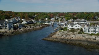 AX147_250 - 6k aerial stock footage approaching oceanfront homes, small bridge, harbor, autumn, Ogunquit, Maine