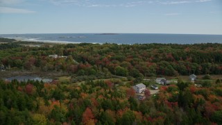 AX147_383E - 6K aerial stock footage flying over rural homes, colorful forest, approaching the beach, Phippsburg, Maine