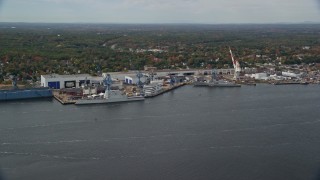 AX147_411E - 6K aerial stock footage flying by waterfront General Dynamics Bath Iron Works, autumn, Bath, Maine