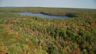 AX148_024 - 6K aerial stock footage flying over a colorful forest, approach Mccurdy Pond, autumn, Damariscotta, Maine
