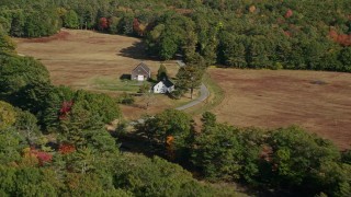 AX148_028 - 6K aerial stock footage flying over colorful forest, approach small farm, barn, autumn, Bremen, Maine