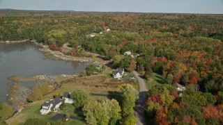 AX148_032E - 6K aerial stock footage flying over forest and rural homes, revealing a pond, autumn, Waldoboro, Maine