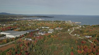 AX148_075E - 6K aerial stock footage flying by forest, warehouse buildings, small coastal town, autumn, Rockland, Maine