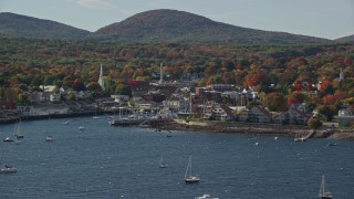 AX148_122 - 6K aerial stock footage flying by small coastal town, boats, autumn, Camden, Maine