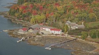 AX148_148E - 6K aerial stock footage flying by boat dealer dock and garage, forest, autumn, Brooklin, Maine