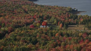 AX148_152E - 6K aerial stock footage flying by rural home, colorful forest in autumn, Brooklin, Maine