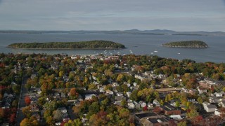 AX148_204E - 5.5K aerial stock footage flying away from harbor and over coastal town with fall foliage, Bar Harbor, Maine