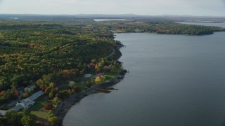 AX148_224 - 5.5K aerial stock footage flying over water toward rode winding through forest with partial fall foliage, Bar Harbor, Maine