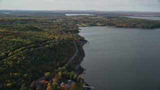 AX148_224E - 5.5K aerial stock footage flying over water toward rode winding through forest with partial fall foliage, Bar Harbor, Maine