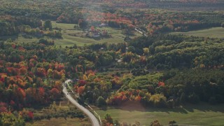 AX148_229 - 5.5K aerial stock footage passing by a road winding through forest toward rural homes, fall foliage, Bar Harbor, Maine