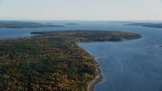 AX149_010 - 5.5K aerial stock footage flying over forest with fall foliage toward the water, autumn, Surry, Maine