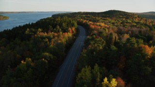 AX149_118 - 5.5K aerial stock footage flying over a road among colorful forest in autumn, Stockton Springs, Maine, sunset