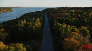 AX149_120 - 5.5K aerial stock footage flying over quiet road among a colorful forest in autumn, Stockton Springs, Maine, sunset