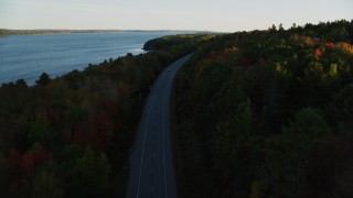 AX149_121 - 5.5K aerial stock footage flying over road with no traffic, colorful forest in autumn, Stockton Springs, Maine, sunset