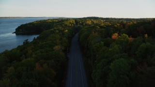 AX149_122 - 5.5K aerial stock footage flying over a road situated among, colorful forest in autumn, Stockton Springs, Maine, sunset