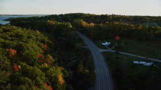 AX149_125 - 5.5K aerial stock footage flying high over quiet road among colorful forest, autumn, Stockton Springs, Maine, sunset