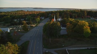AX149_127E - 5.5K aerial stock footage following road past church and cemetery, autumn, Stockton Springs, Maine, sunset