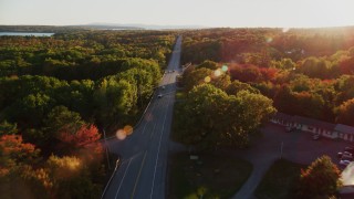 AX149_128 - 5.5K aerial stock footage flying over road, colorful trees in autumn, Stockton Springs, Maine, sunset