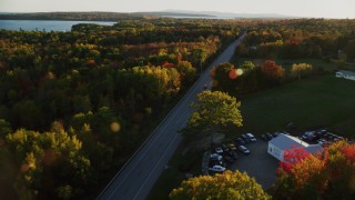 AX149_130 - 5.5K aerial stock footage tracking car on road through forest in autumn, Stockton Springs, Maine, sunset