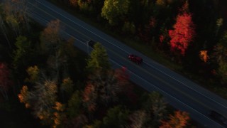 AX149_135 - 5.5K aerial stock footage tracking car on road through forest in autumn, Stockton Springs, Maine, sunset
