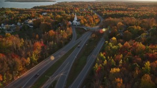 AX149_135E - 5.5K aerial stock footage tracking car on road through forest in autumn, Stockton Springs, Maine, sunset
