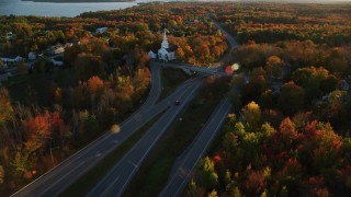 AX149_137 - 5.5K stock footage aerial video tracking car on road by near a white church, autumn, Stockton Springs, Maine, sunset