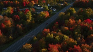 AX149_139 - 5.5K aerial stock footage tracking car on road through small town nestled among trees, autumn, Stockton Springs, Maine, sunset