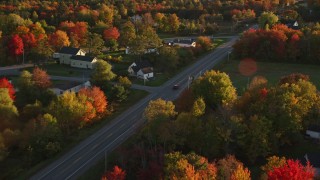 AX149_139E - 5.5K aerial stock footage tracking car on road through small town nestled among trees, autumn, Stockton Springs, Maine, sunset