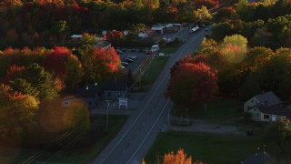 AX149_143 - 5.5K aerial stock footage tracking car on road through small town, autumn, Stockton Springs, Maine, sunset