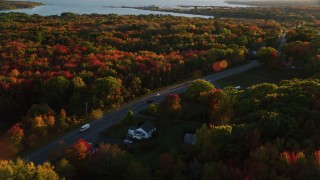 AX149_145 - 5.5K aerial stock footage tracking car on road passing through small town, and trees, autumn, Stockton Springs, Maine, sunset