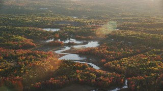 AX149_155 - 5.5K aerial stock footage flying high over a pond, colorful forest in autumn, Belfast, Maine, sunset